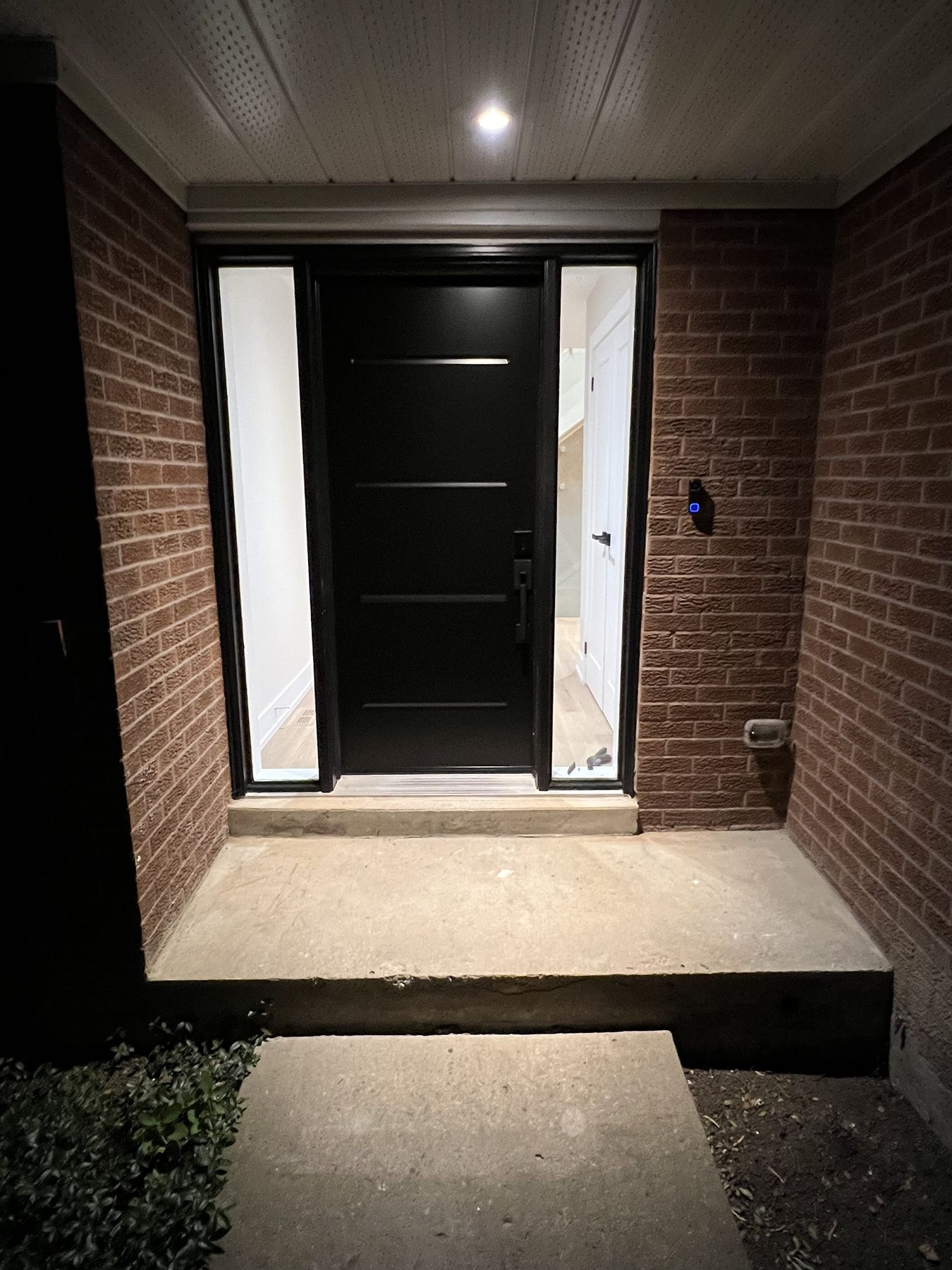 New black front door with sidelights, a lit porch ceiling and stone steps at night